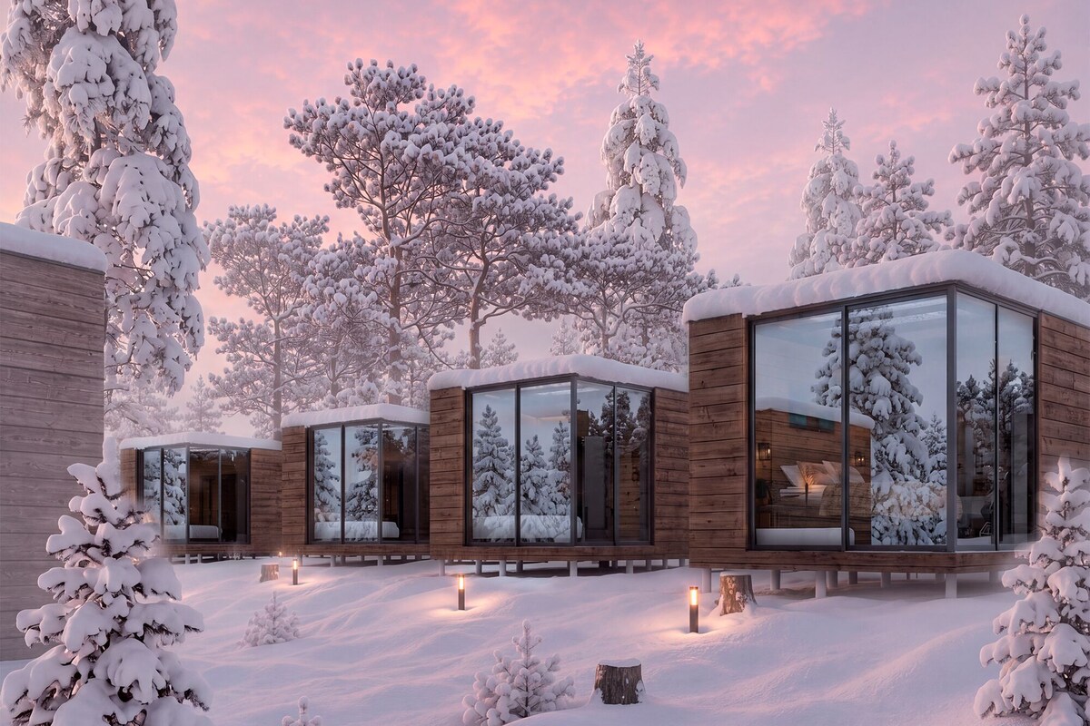 A modern cabin with large glass windows, surrounded by snow-covered trees and a wooden exterior.