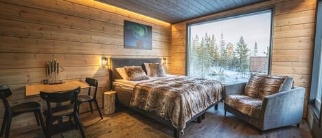 Un dormitorio acogedor con detalles de madera, un ventanal grande, una cama, un sillón y una mesita con velas.