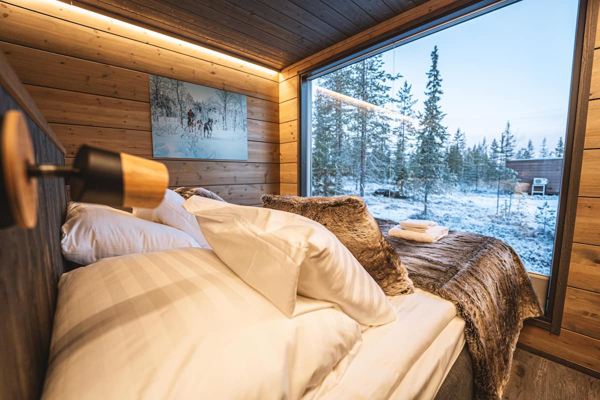 Un dormitorio acogedor con una ventana grande, paredes de madera y una cama con ropa de cama blanca.