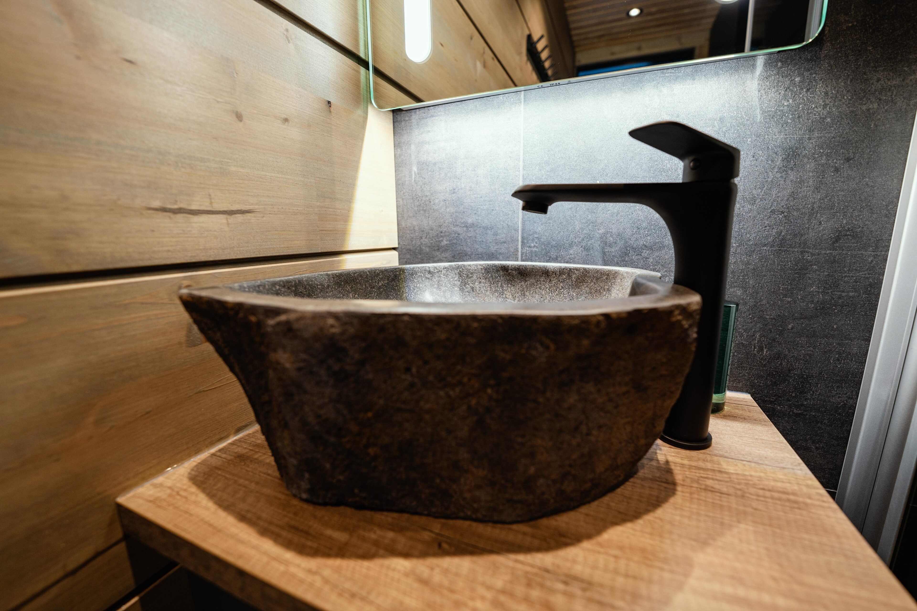 Ein Steinwaschbecken mit modernem Wasserhahn in einem Badezimmer mit Holzvertäfelung.