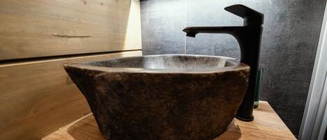 Ein Steinwaschbecken mit modernem Wasserhahn in einem Badezimmer mit Holzvertäfelung.