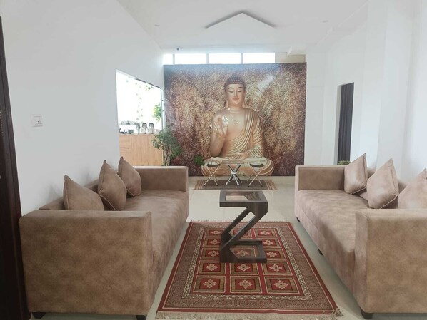 A modern living room with two sofas, a large Buddha statue mural, and a geometric rug. - SS HOTELS (Bengaluru)