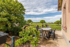 Une terrasse avec une table et des chaises, entourée de verdure et offrant une vue sur un champ.