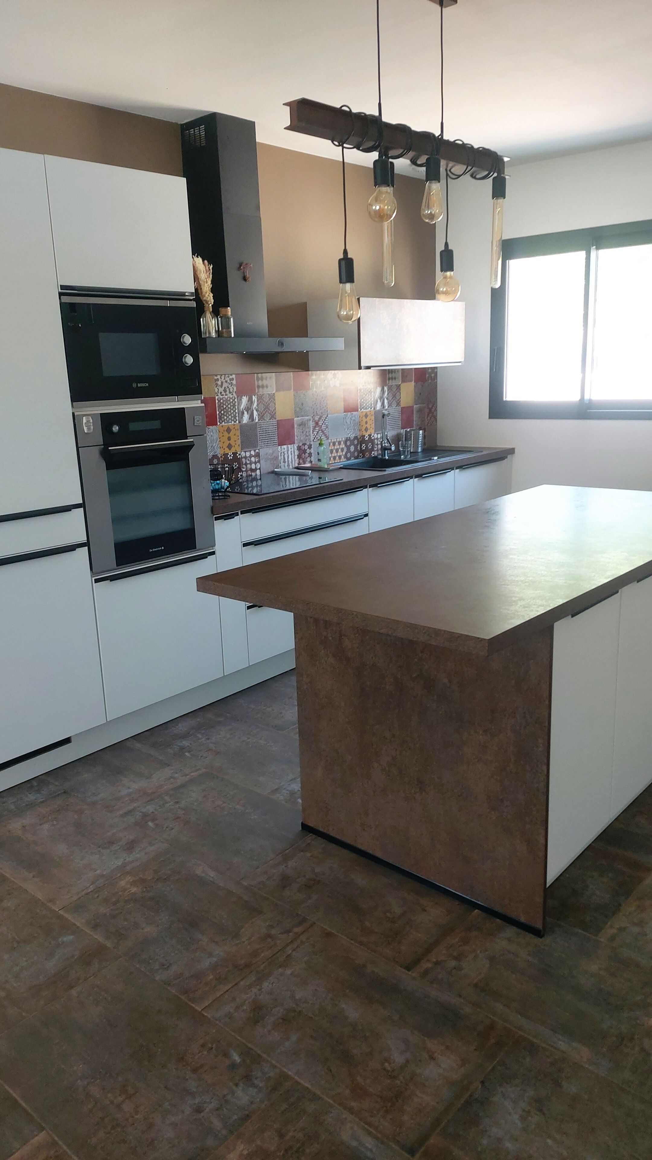 A modern kitchen with a central island, built-in ovens, and hanging pendant lights.