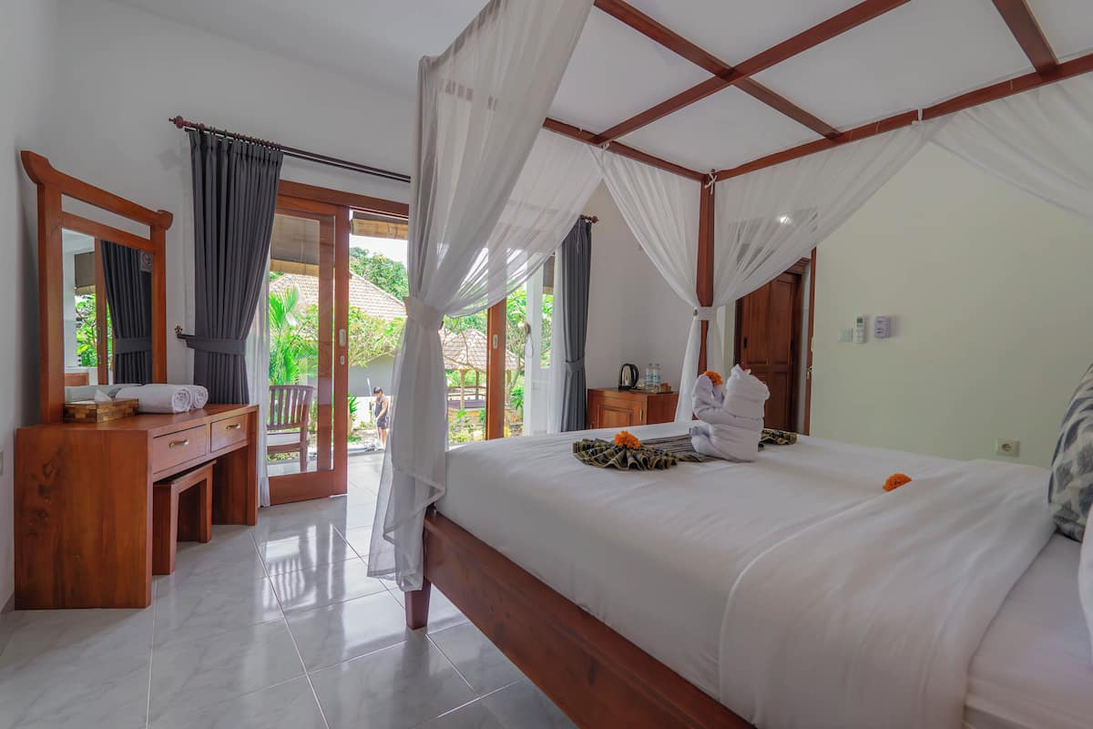 A bedroom with a four-poster bed, wooden desk, and a view of the outdoors.