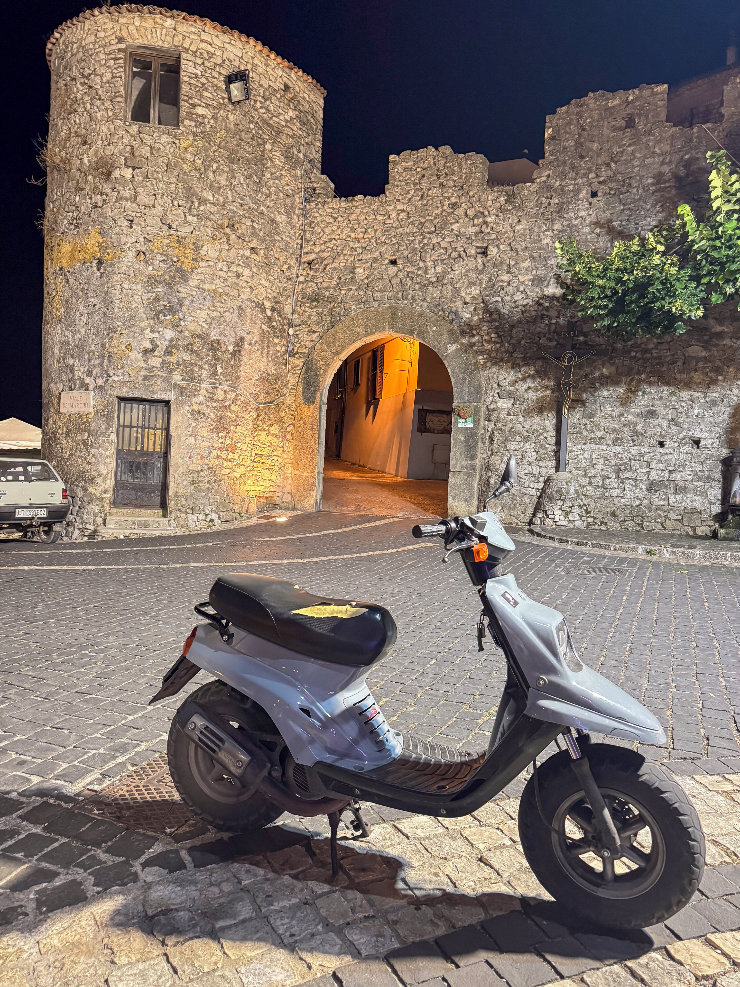 A scooter parked in front of a stone building with an arched entrance.