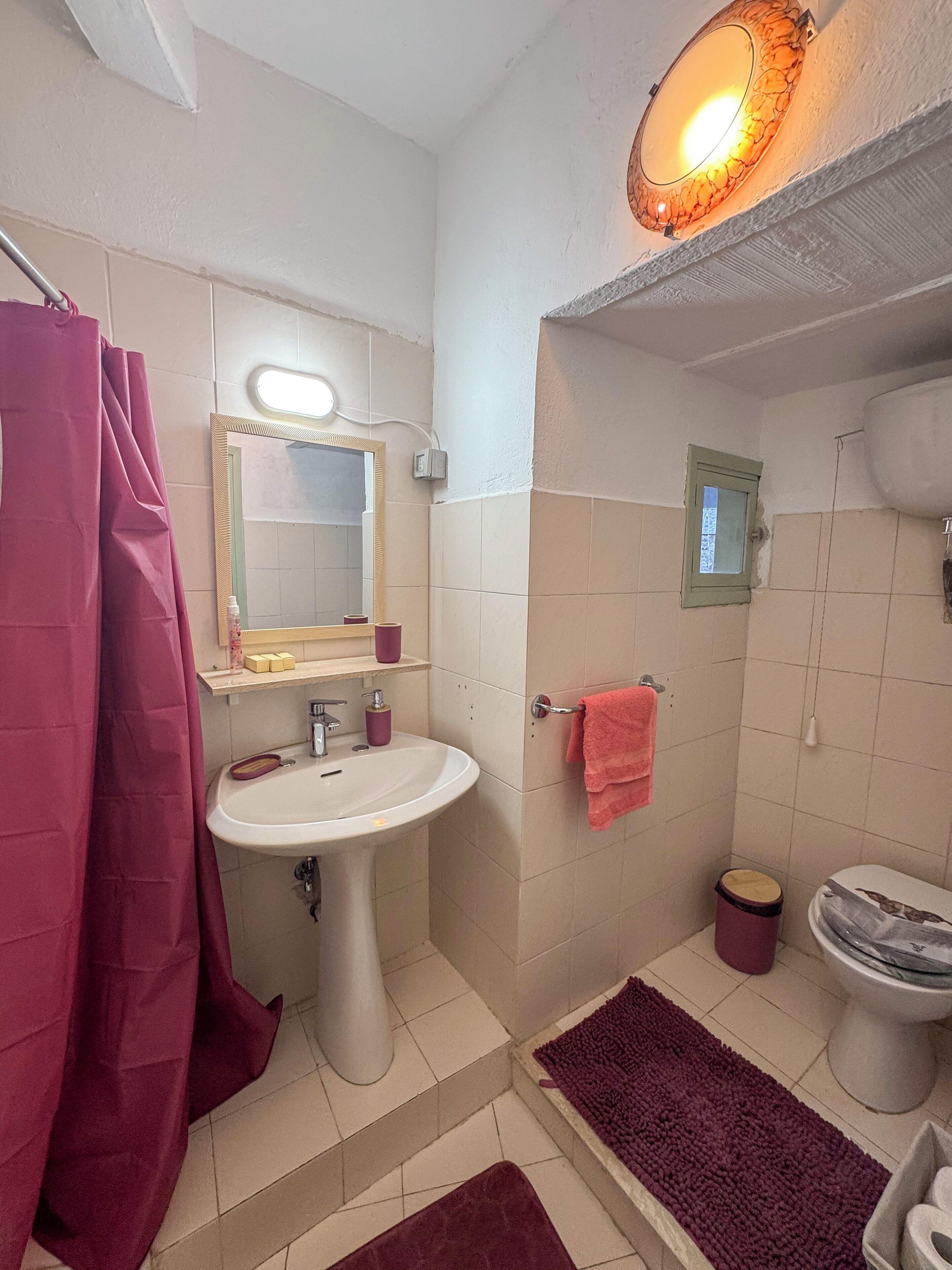 A bathroom with a sink, mirror, and toilet. There is a shower curtain, a bath mat, and a towel rack.
