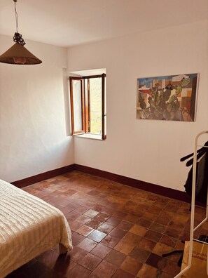 A room with a bed, a window with curtains, a painting on the wall, and a tiled floor. - Historic & Charming Home in Bassiano (Bassiano)