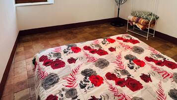 A bedroom with a bed, a window, a painting, a standing fan, and a heater.