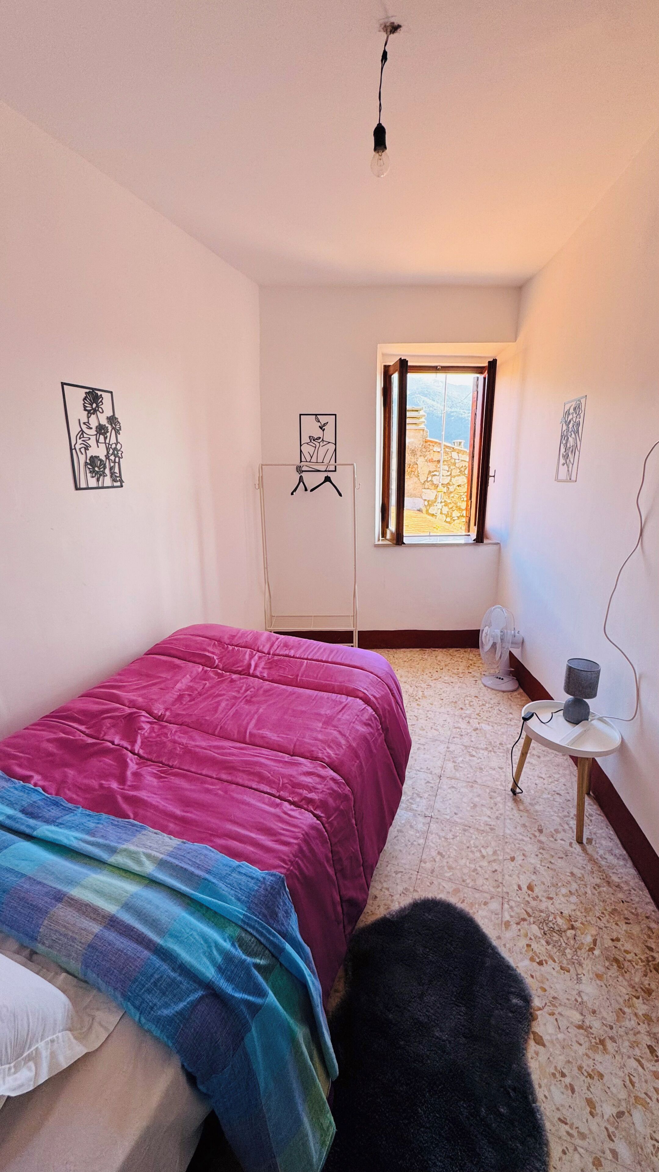Una camera da letto con un letto, una ventola da terra, una finestra e opere d'arte alle pareti.