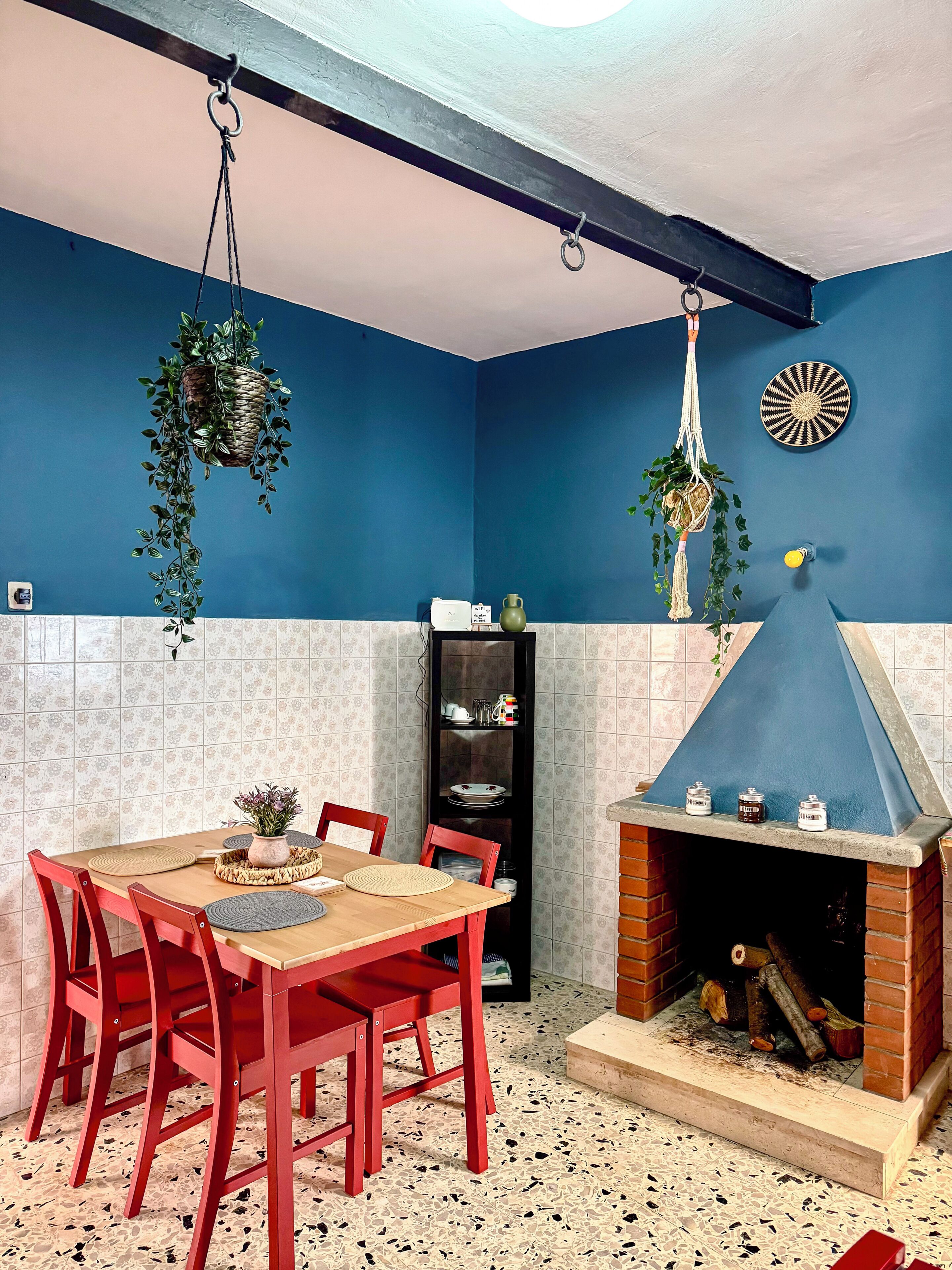 Ein Essbereich mit einem Holztisch, roten Stühlen, einer blauen Wand und einem Kamin mit Holzscheiten.