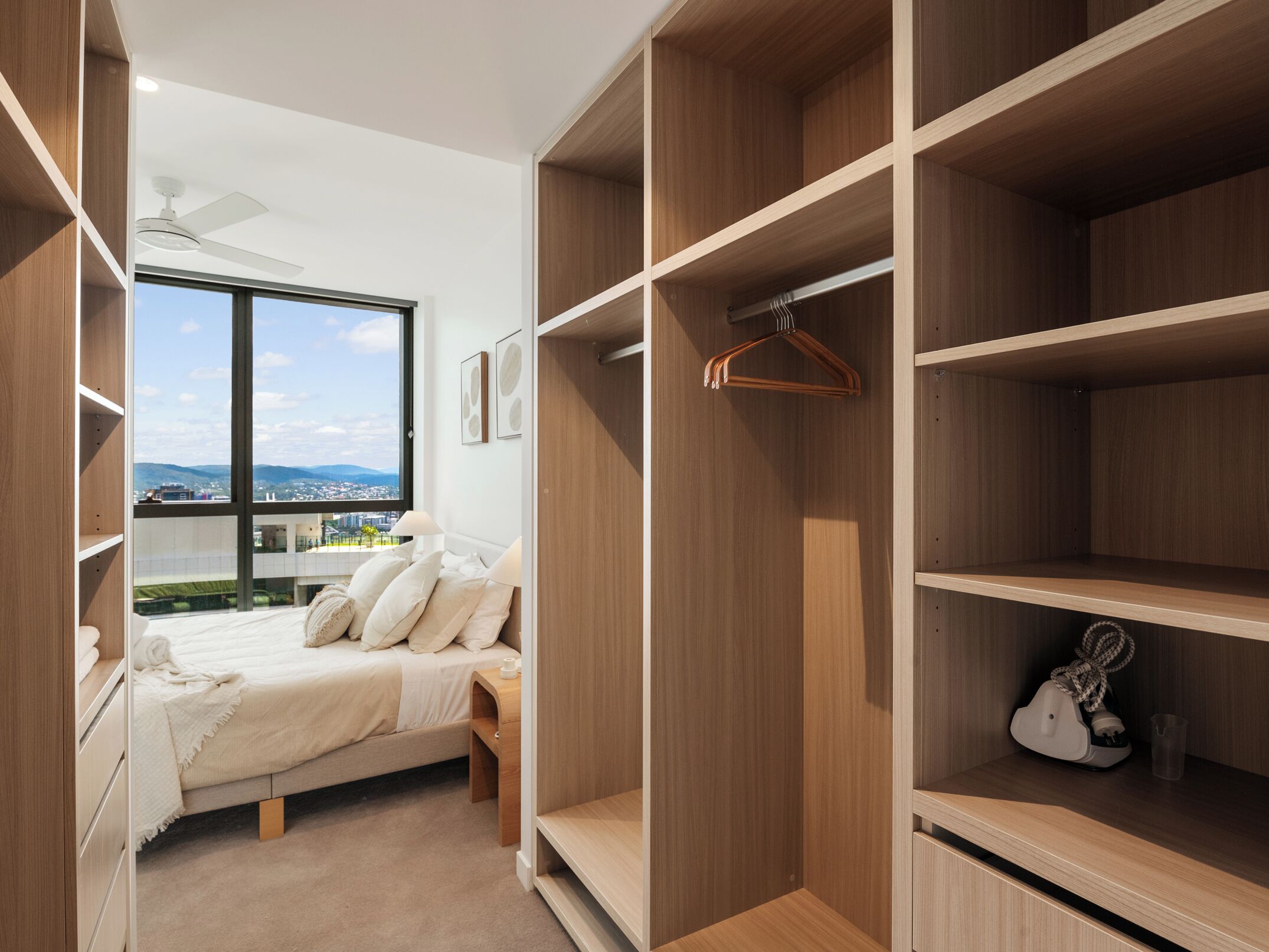 A modern bedroom with a large window, a bed, and built-in wooden shelving.