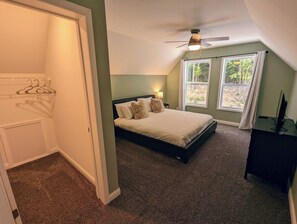 Un dormitorio con cama, ventilador de techo, televisor y ventana con cortinas.