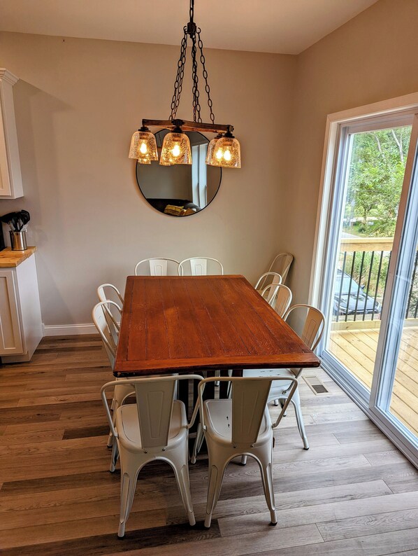 Un comedor con mesa de madera y sillas blancas, una lámpara colgante y un espejo grande en la pared.