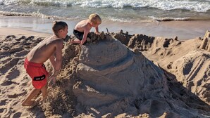 Two children building a sandcastle on a beach with waves in the background.