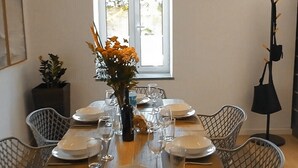 A dining area with a wooden table set for four, surrounded by wire mesh chairs, under a pendant light.