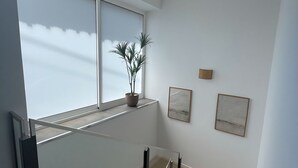A modern staircase with glass railings, wooden flooring, and a potted plant on the landing.