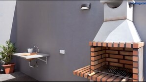 A modern outdoor kitchen with a brick grill, a sink, and a small countertop.