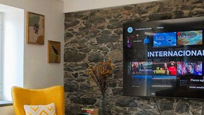 A living room with a stone wall, a yellow armchair, a white entertainment unit, and a flat-screen TV displaying a movie selection.