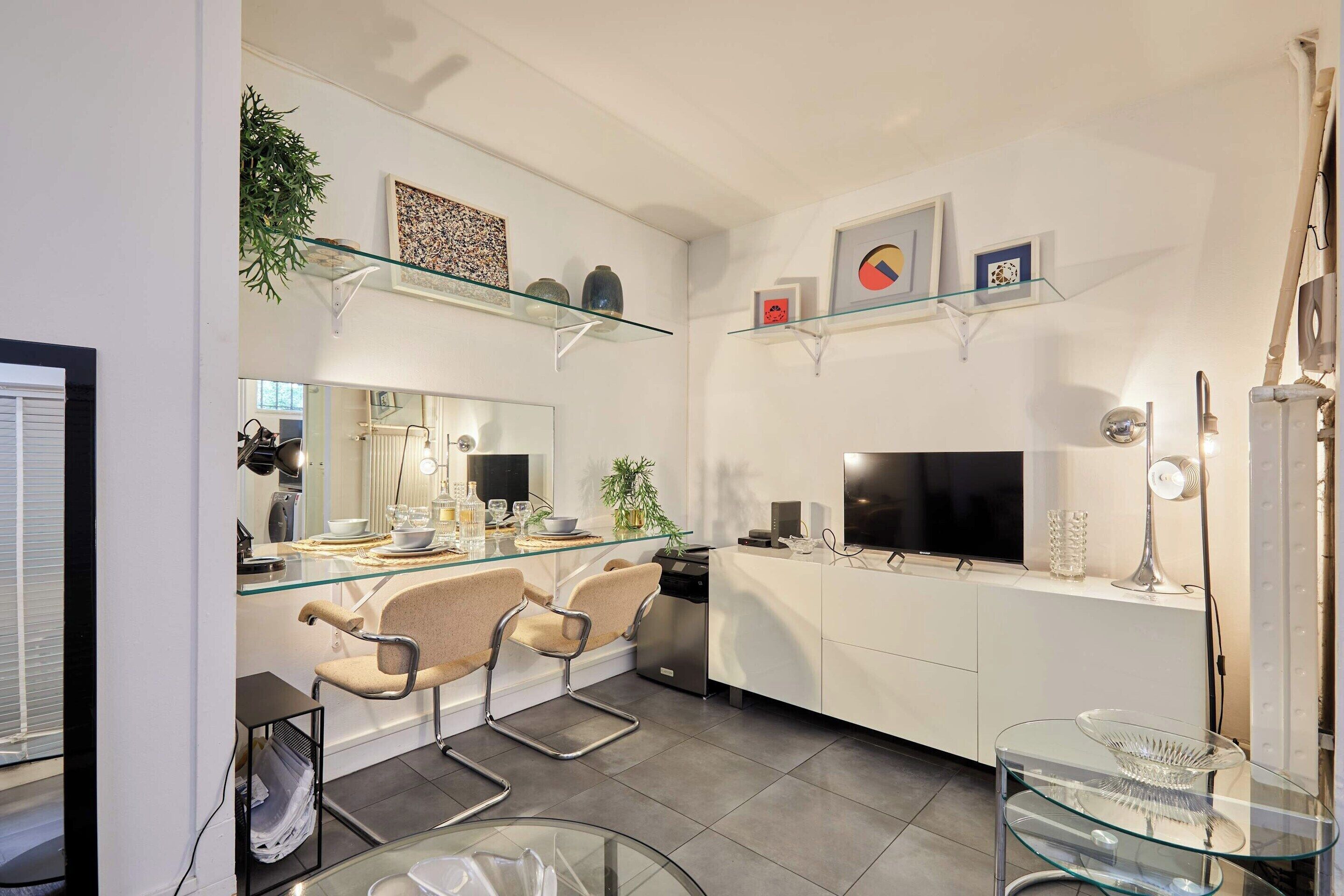 A modern kitchen with a glass dining table, bar stools, a built-in oven, and a TV.