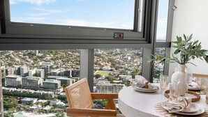 A high-rise room with a city view, a round table set with plates and glasses, and a wicker chair. - Million$ Panoramic RiverView/ Casino/ Designer/CBD (Brisbane)