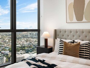 Una camera da letto con un'ampia finestra, un letto con testiera trapuntata e un comodino con una lampada.