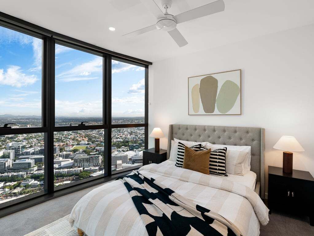 Camera da letto con una grande finestra, un letto, una ventola a soffitto e vista sulla città.