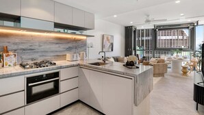 A modern kitchen with a marble countertop, integrated oven, and a dining area with a sofa and coffee table. - Million$ Panoramic RiverView/ Casino/ Designer/CBD (Brisbane)