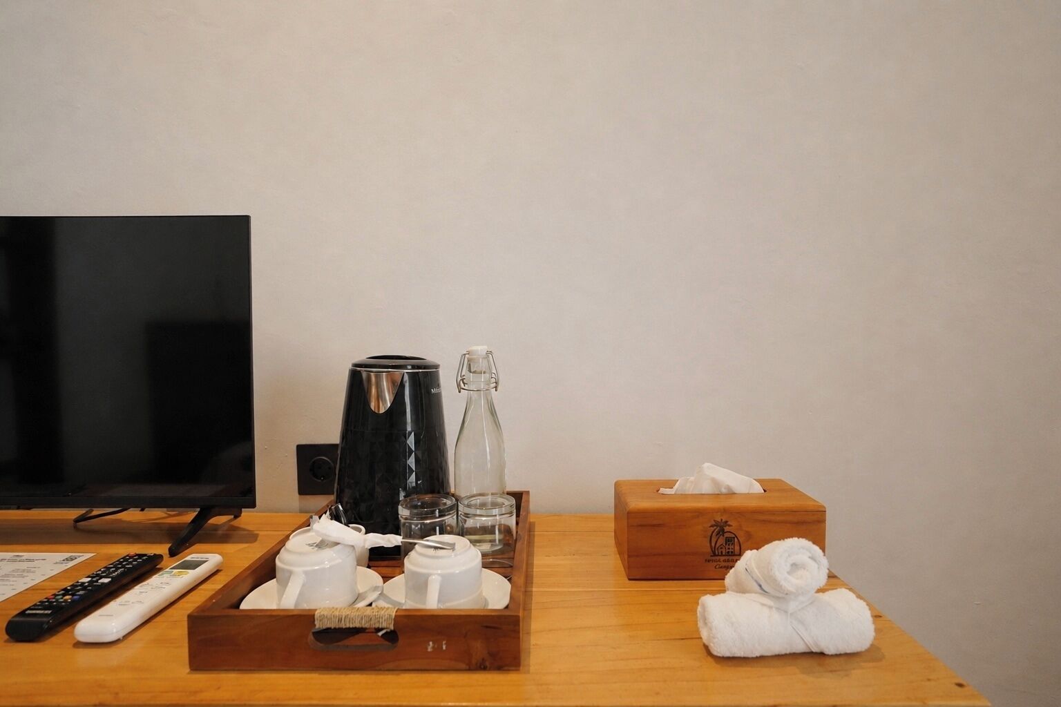 A hotel room with a TV, a coffee maker, a bottle, a tissue box, a remote control, and a tray with cups and a spoon.