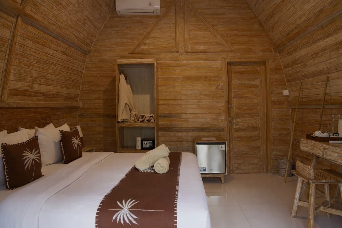 A wooden room with a bed, a shelf with towels, a small table, and a heater.