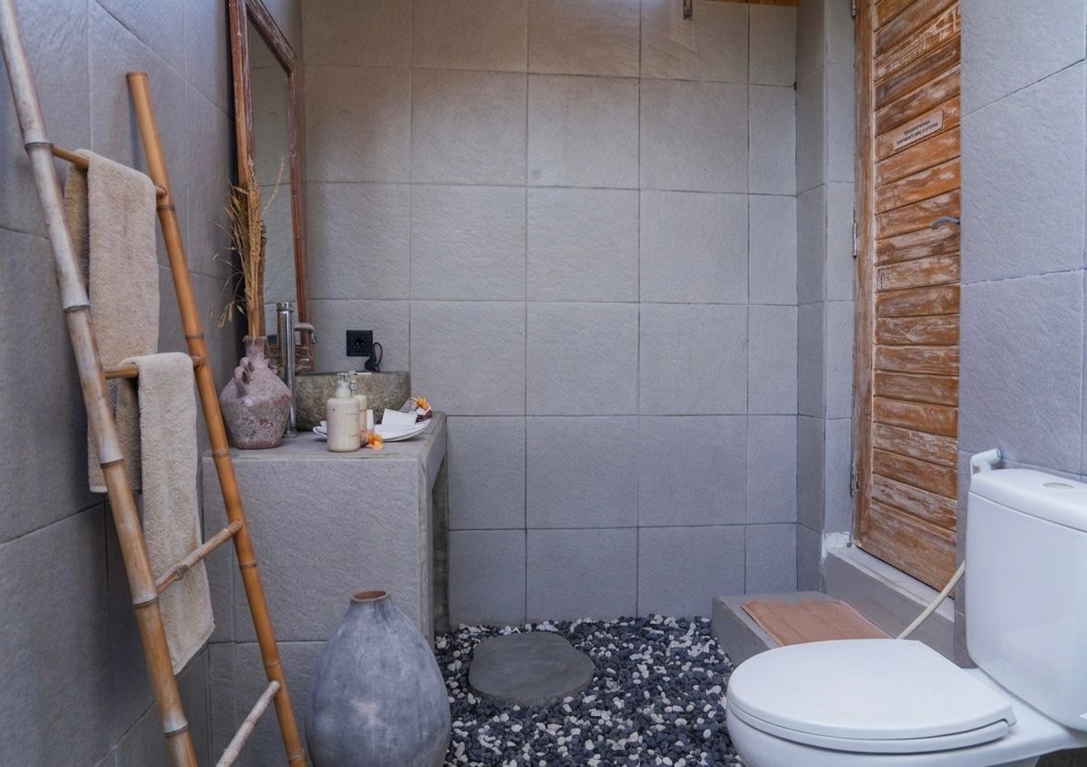 A small bathroom with a toilet, a bamboo ladder, a mirror, and a stone sink.