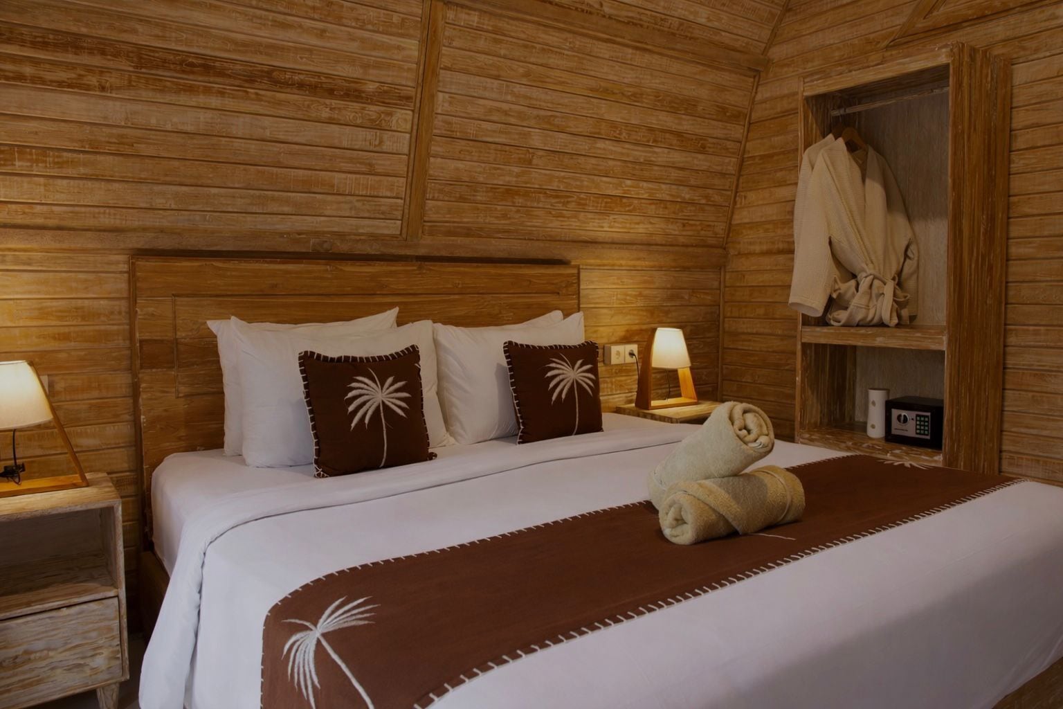 Une pièce en bois avec un lit, des oreillers, une table de chevet, une lampe, un peignoir et une serviette.