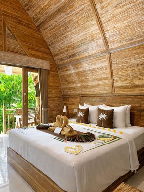 Une pièce avec un plafond en bois, un lit recouvert de draps blancs et une vue sur la verdure à l’extérieur.
