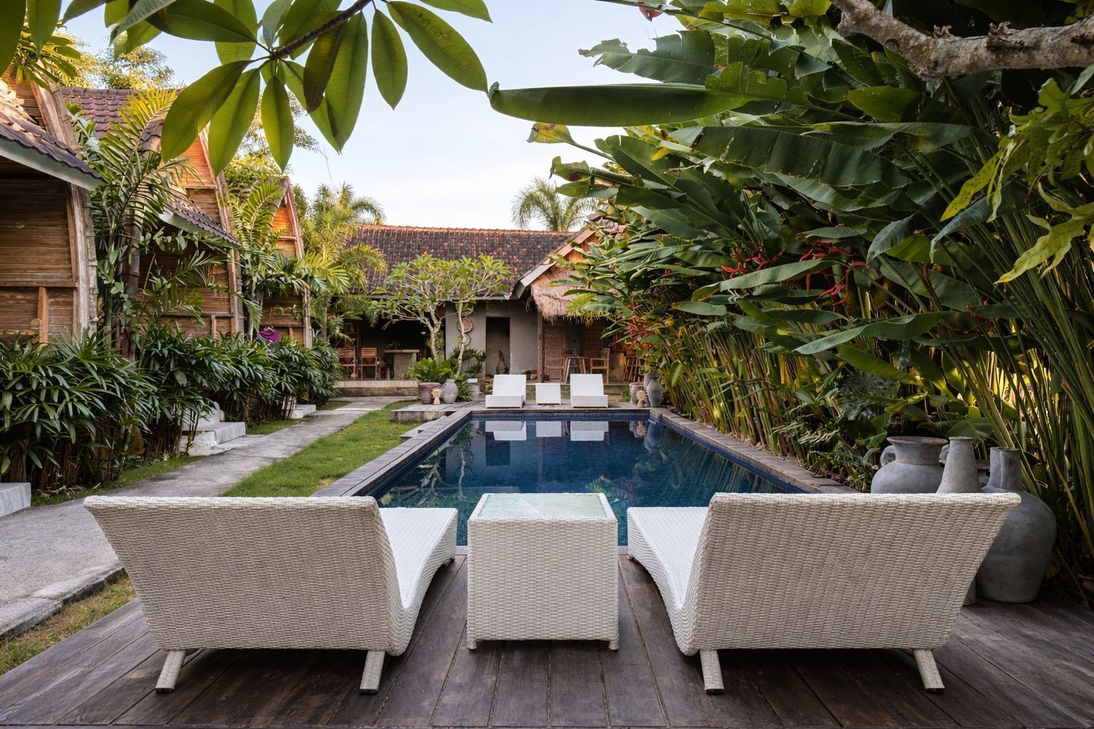 A pool area with wicker furniture and tropical plants.
