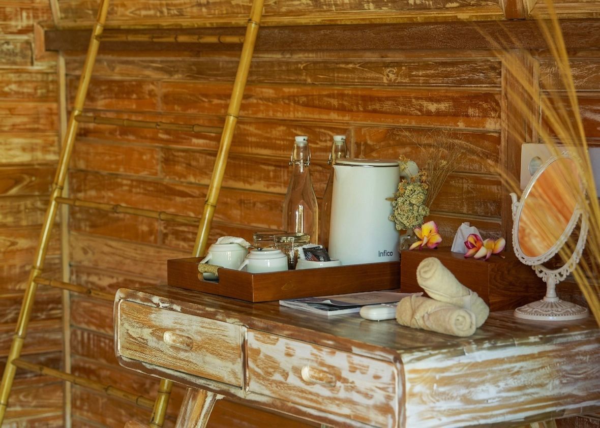 Una pared de madera con una escalera de madera, una tetera blanca, una botella, un recipiente blanco pequeño, un espejo y una toalla sobre un aparador de madera.