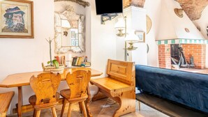 Een knus vertrek met een houten tafel, stoelen, een bank, een televisie en een open haard.