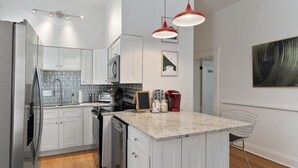 Une cuisine moderne avec des meubles blancs, un plan de travail en granit et un îlot central doté de tabourets de bar.
