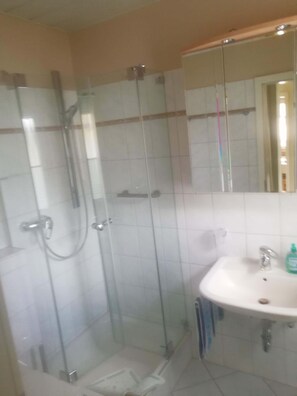 Un baño con ducha de vidrio, un lavabo blanco y un espejo sobre él.