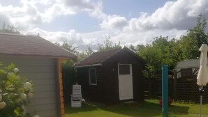 Een klein houten vakantiehuisje met pannendak, omringd door een gazon en een houten hek.