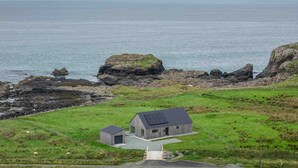 A coastal house with a large garage and a smaller attached structure, surrounded by grassy fields and rocky coastline. - Wow sea-view! walks, cliffs, wildlife - spacious contemporary home (Portree)