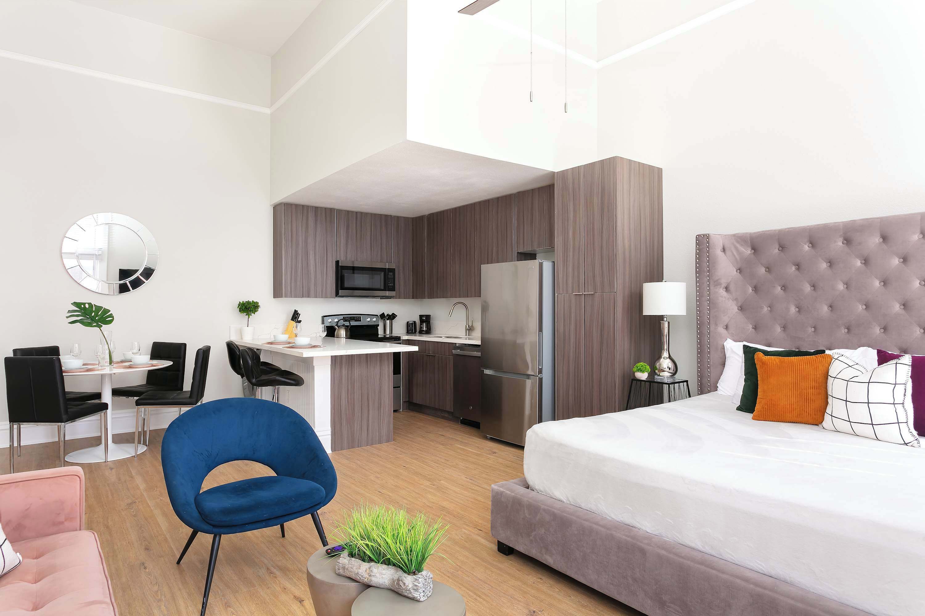 A modern hotel room with a large bed, a small kitchenette, a dining area, and a living space.