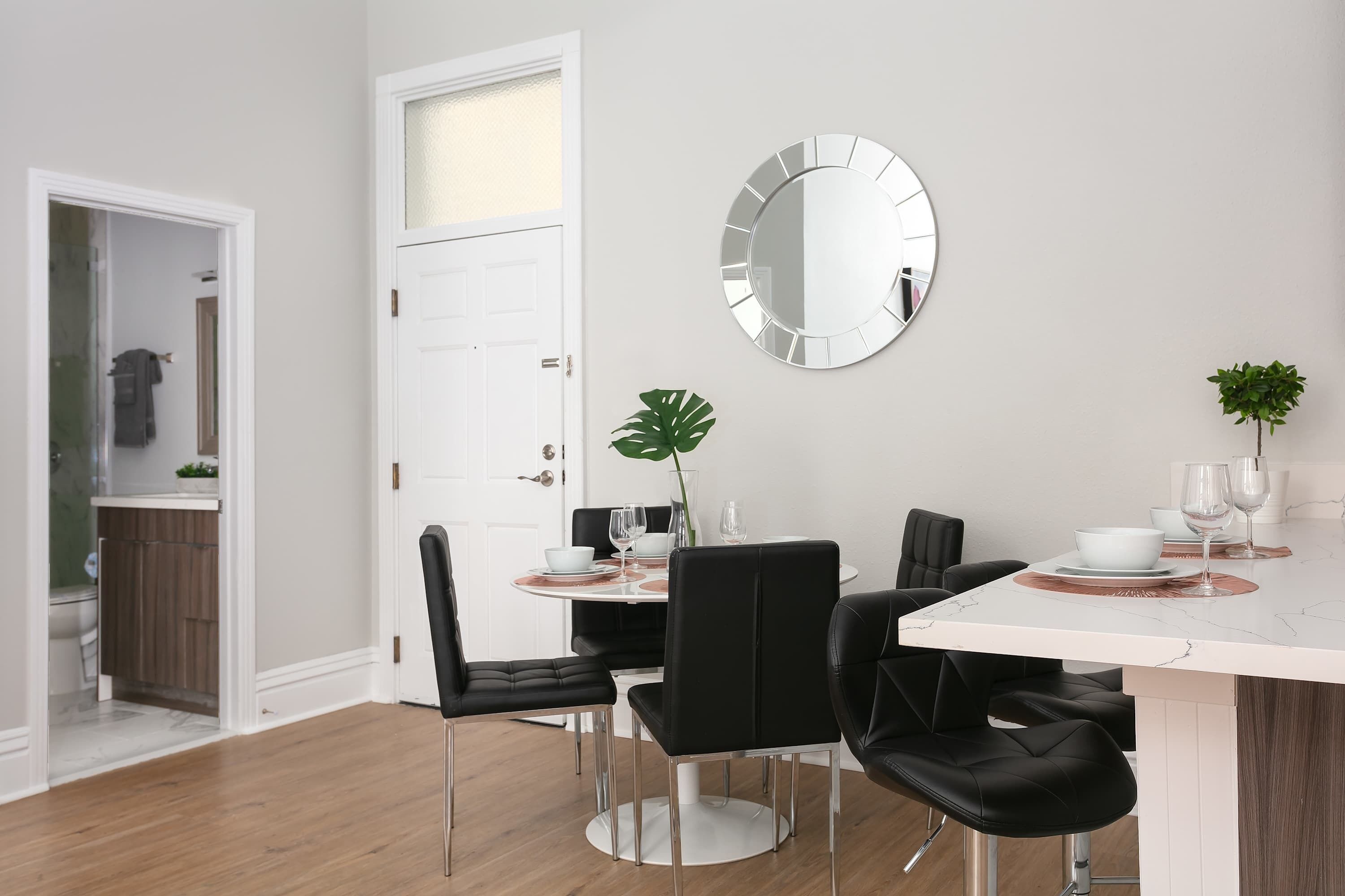 Un comedor moderno con una mesa de mármol blanco, sillas negras y un espejo grande en la pared.