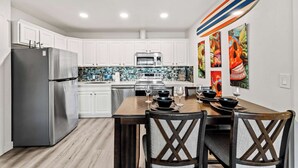 Una cocina moderna con armarios blancos, electrodomésticos de acero inoxidable, una mesa de comedor de madera y coloridas obras de arte en la pared.