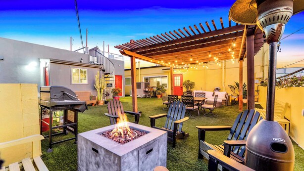 Un patio exterior con una chimenea, sillas Adirondack, una pérgola con luces y una parrilla.