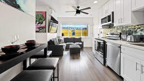 A modern kitchen with white cabinets, stainless steel appliances, and a dining area with a grey sofa and black dining set. - 2BR Urban Retreat w/ Rooftop Lounge (San Diego)