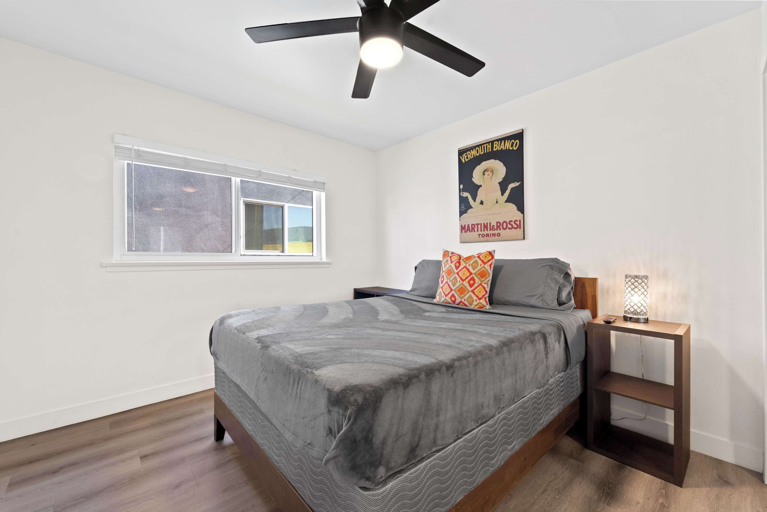 A bedroom with a bed, a nightstand, a ceiling fan, a window, and a poster on the wall.