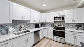 A modern kitchen with white cabinets, a stainless steel dishwasher, a built-in oven, and a microwave.