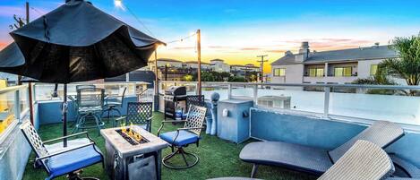 A rooftop patio with outdoor furniture, a grill, and a large umbrella.