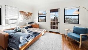 Un dormitorio con una cama, una silla, una mesita, una ventana y una puerta.