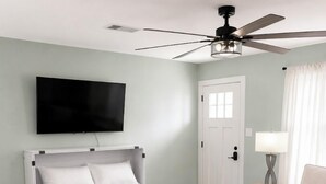 Una habitación de hotel moderna con cama, ventilador de techo, televisor, puerta, lámpara y sofá.